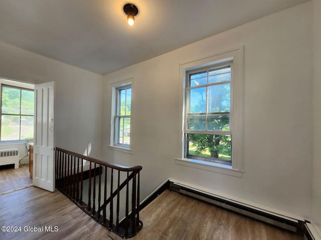 stairway with radiator, a wealth of natural light, a baseboard radiator, and hardwood / wood-style flooring