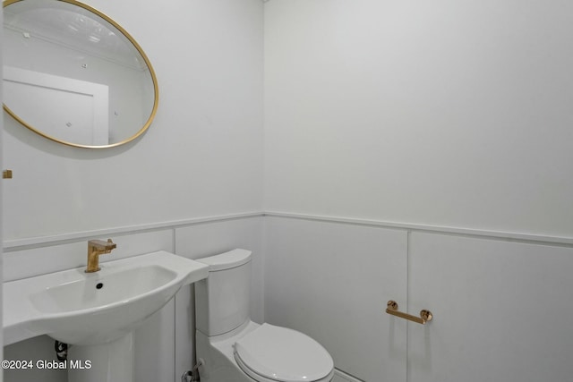 half bathroom with a sink, a wainscoted wall, toilet, and a decorative wall