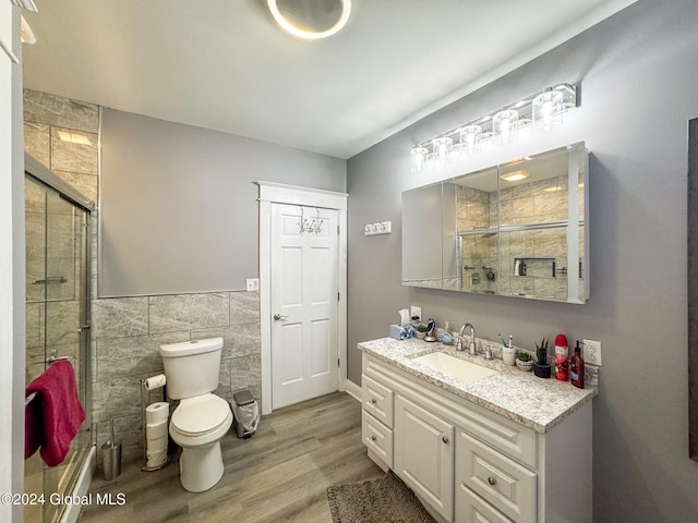 bathroom featuring hardwood / wood-style floors, vanity, a shower with door, toilet, and tile walls