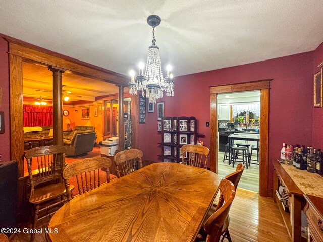 dining area featuring a textured ceiling, an inviting chandelier, decorative columns, and light hardwood / wood-style flooring