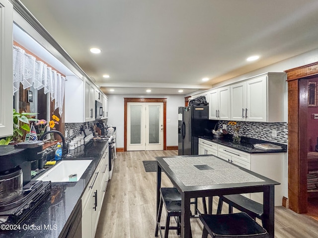 kitchen with backsplash, white cabinets, sink, appliances with stainless steel finishes, and light hardwood / wood-style floors