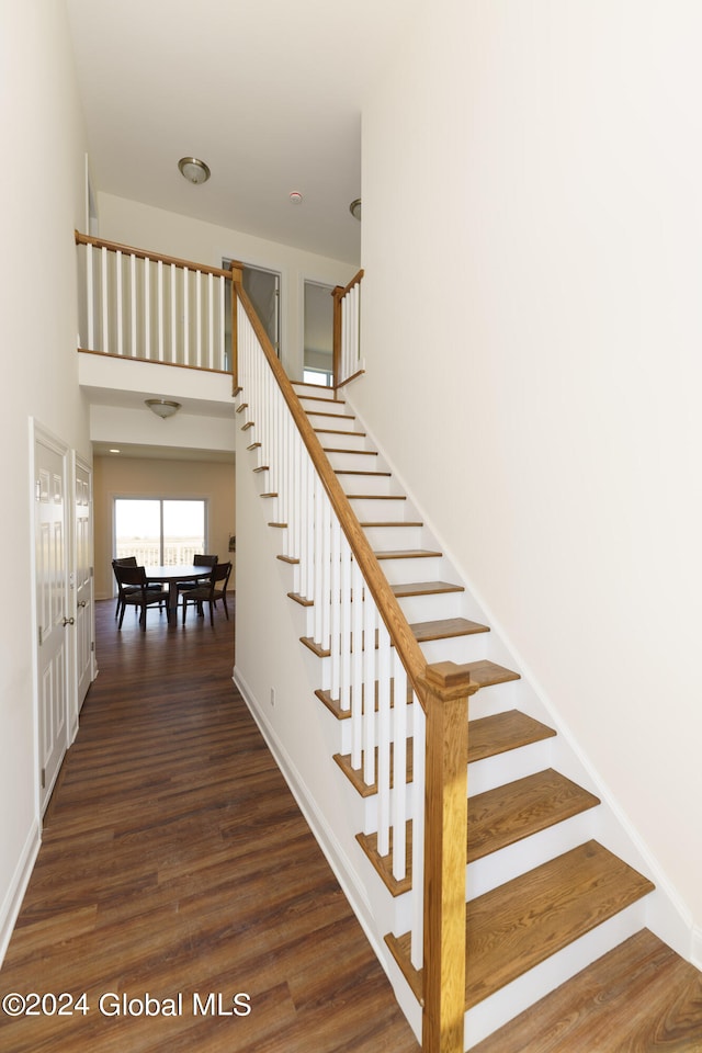 stairs with a towering ceiling and wood-type flooring