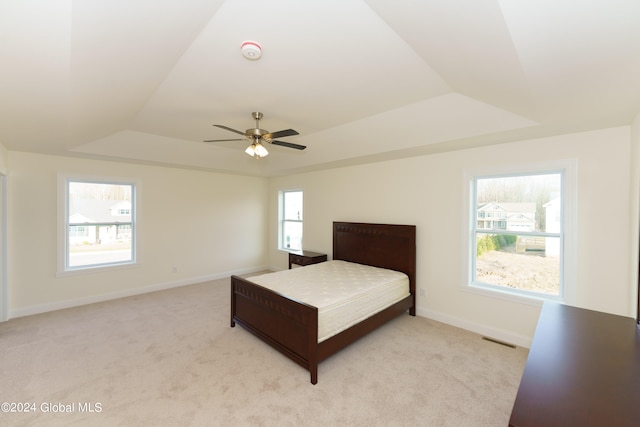 bedroom featuring light carpet, a raised ceiling, and ceiling fan