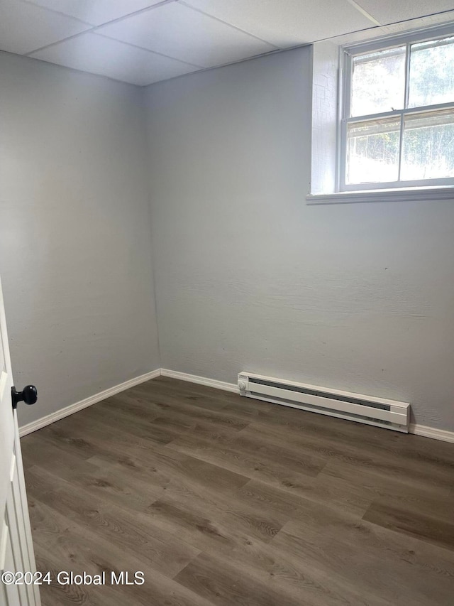 unfurnished room with dark hardwood / wood-style floors, a baseboard heating unit, and a drop ceiling