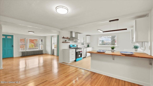 kitchen featuring stainless steel appliances, radiator heating unit, white cabinets, wall chimney exhaust hood, and light hardwood / wood-style flooring