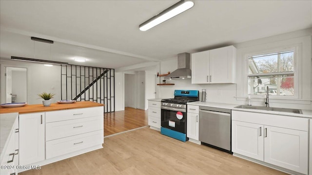 kitchen featuring sink, appliances with stainless steel finishes, wall chimney exhaust hood, light hardwood / wood-style flooring, and white cabinets