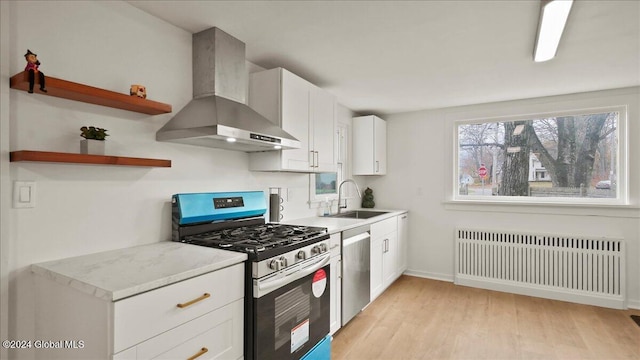 kitchen featuring radiator, stainless steel appliances, light wood-type flooring, wall chimney range hood, and sink