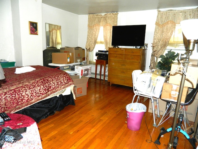 bedroom with baseboard heating, dark hardwood / wood-style flooring, and multiple windows