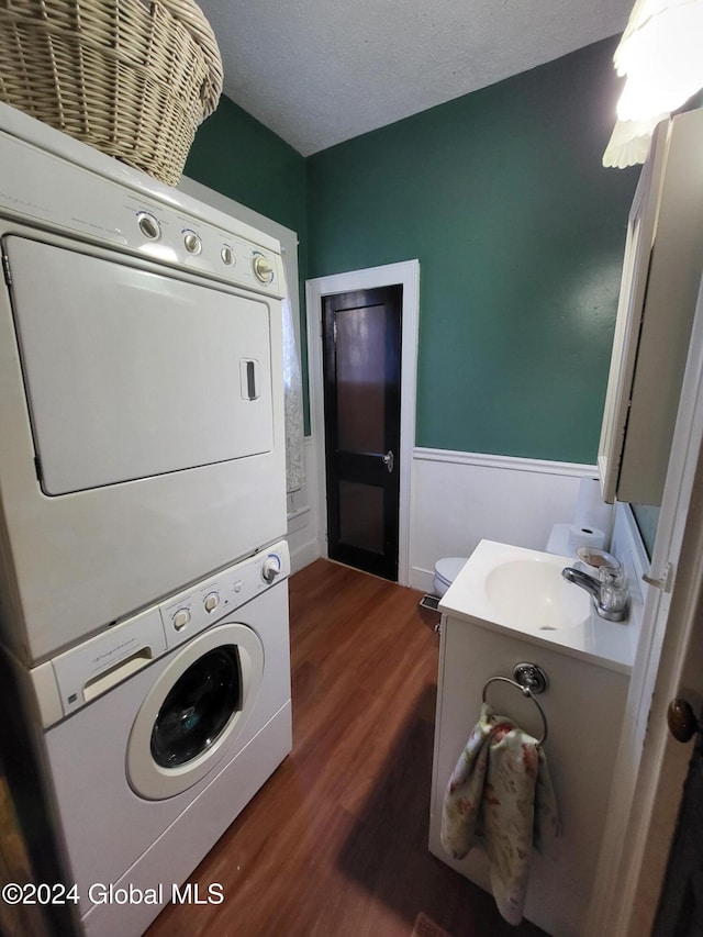 washroom featuring sink, stacked washing maching and dryer, a textured ceiling, and dark hardwood / wood-style floors