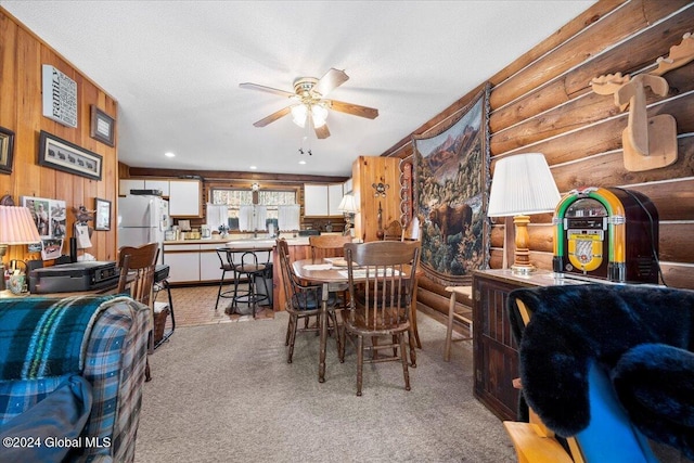 dining area featuring light carpet, wooden walls, ceiling fan, and a textured ceiling