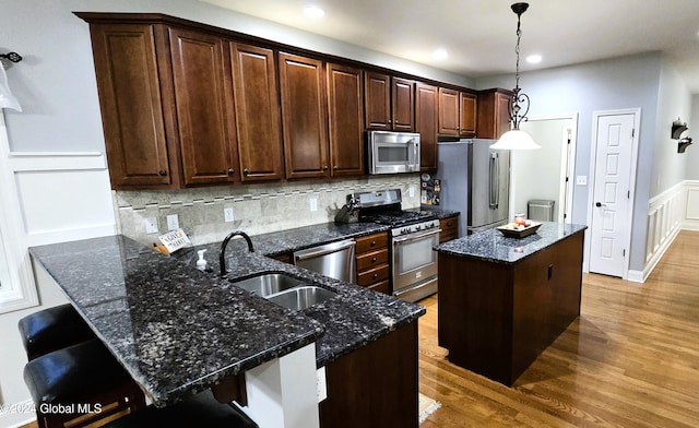 kitchen with appliances with stainless steel finishes, a breakfast bar, hardwood / wood-style floors, a center island, and hanging light fixtures