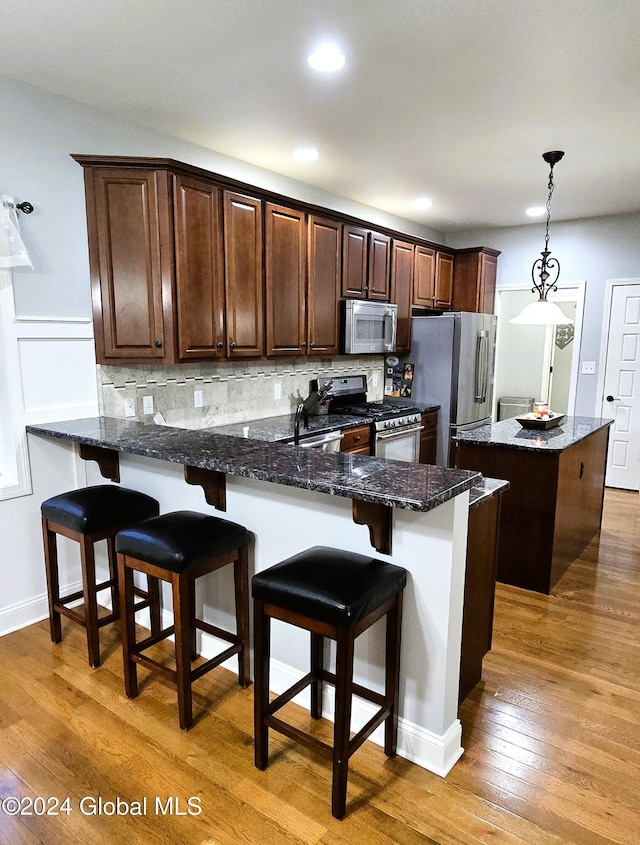 kitchen featuring pendant lighting, wood-type flooring, appliances with stainless steel finishes, and dark stone counters