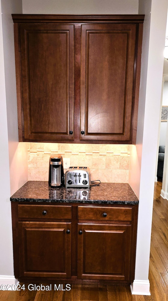 kitchen featuring dark brown cabinets, dark hardwood / wood-style floors, tasteful backsplash, and dark stone counters