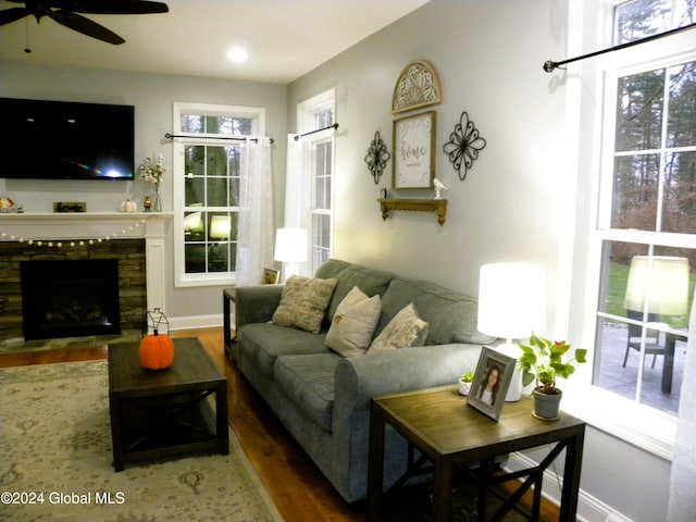 living room featuring a stone fireplace, ceiling fan, and dark wood-type flooring