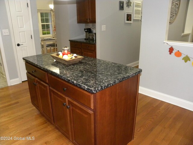 kitchen with a center island, light hardwood / wood-style floors, hanging light fixtures, and dark stone countertops