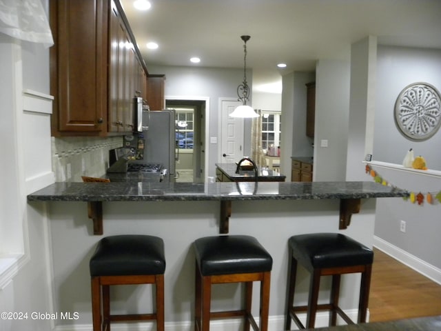 kitchen with a kitchen bar, tasteful backsplash, dark wood-type flooring, and hanging light fixtures