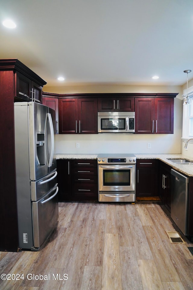 kitchen featuring light stone counters, light hardwood / wood-style flooring, sink, pendant lighting, and appliances with stainless steel finishes