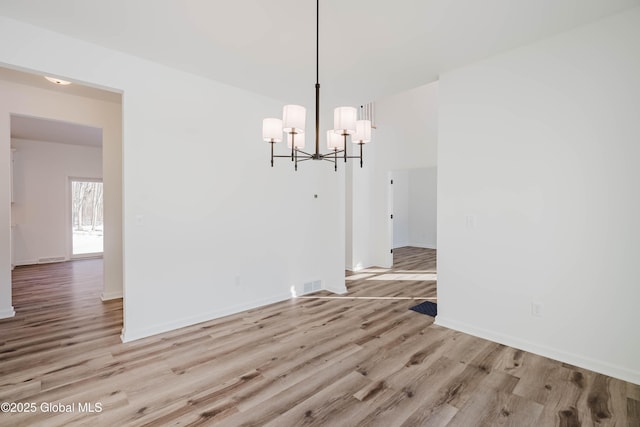 unfurnished dining area featuring an inviting chandelier and light hardwood / wood-style flooring