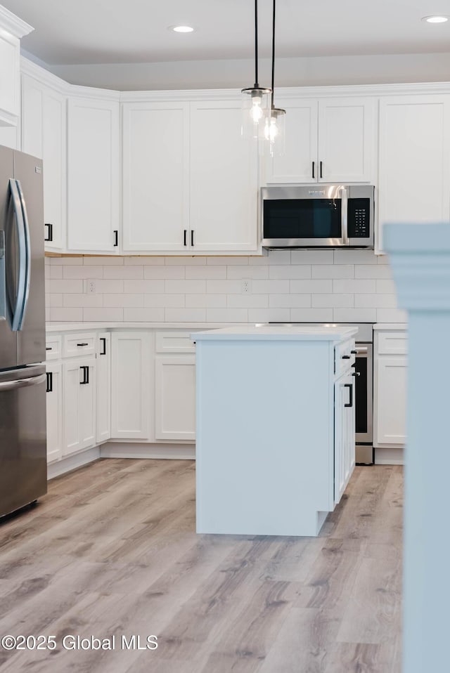 kitchen featuring hanging light fixtures, stainless steel appliances, light hardwood / wood-style floors, white cabinets, and decorative backsplash