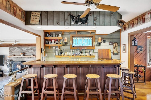 bar featuring decorative backsplash, wood walls, ceiling fan, and light wood-type flooring