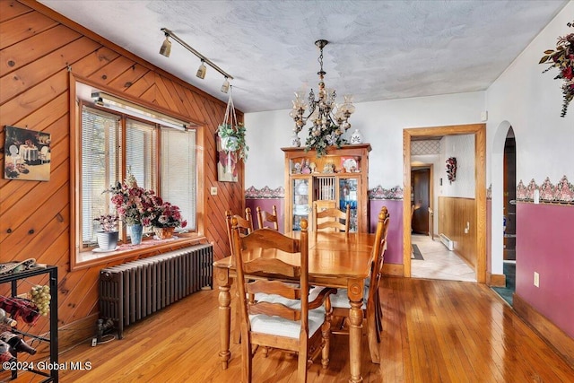 dining area featuring wood walls, radiator heating unit, and light hardwood / wood-style flooring