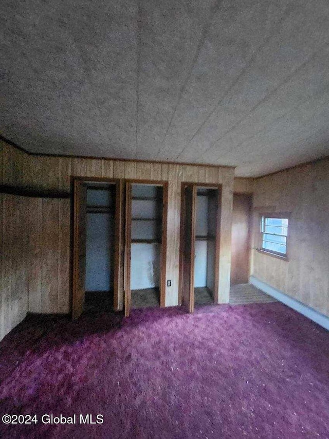 unfurnished bedroom with multiple closets, wood walls, and carpet floors