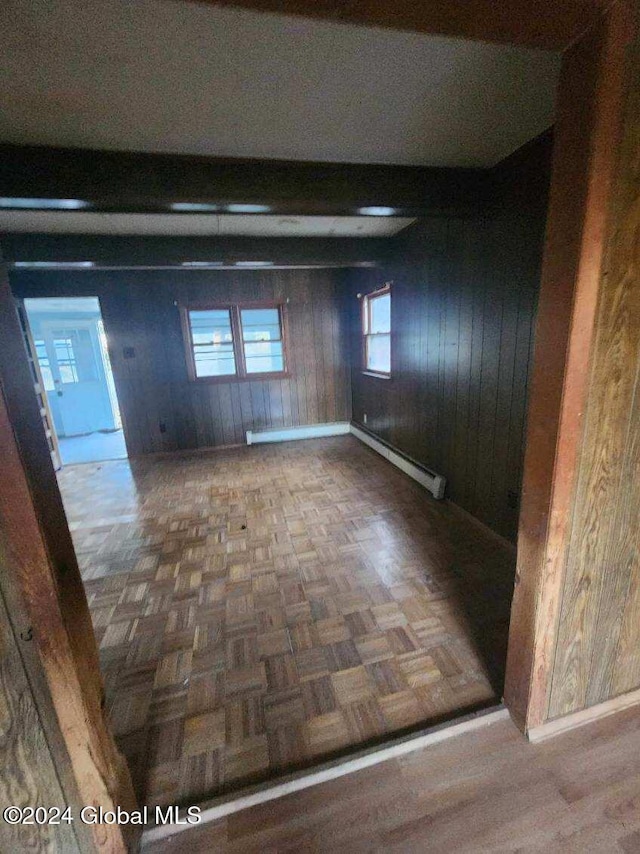 unfurnished room with dark parquet floors, wooden walls, and a baseboard heating unit