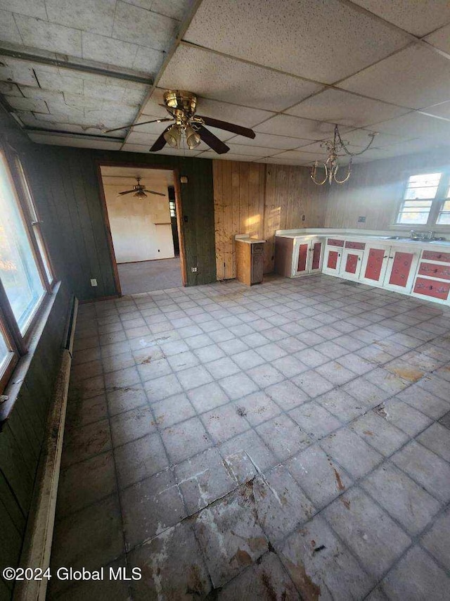 interior space with a drop ceiling, wooden walls, and ceiling fan