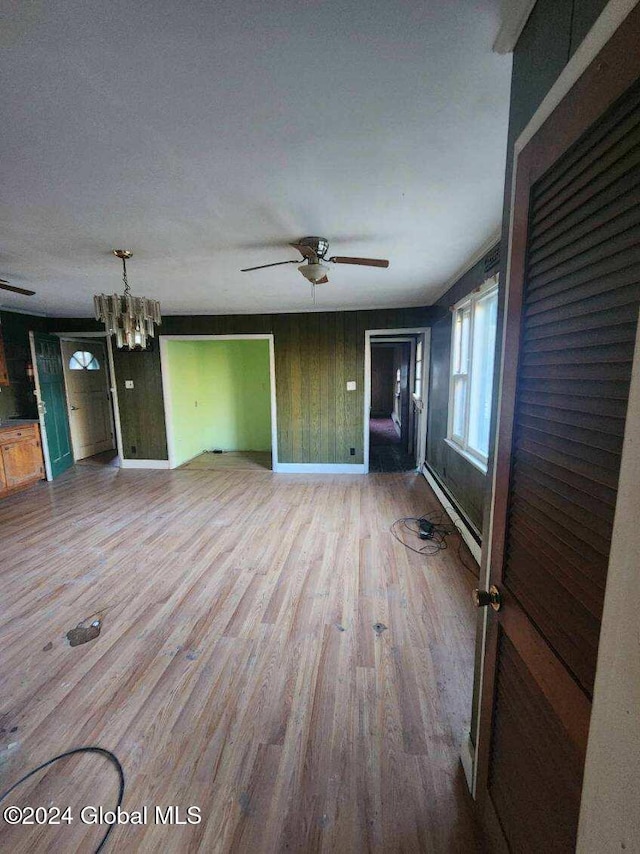 unfurnished living room featuring hardwood / wood-style flooring, ceiling fan with notable chandelier, a textured ceiling, wooden walls, and a baseboard radiator