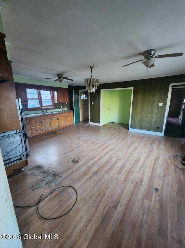 unfurnished living room with wood walls, ceiling fan with notable chandelier, and wood-type flooring