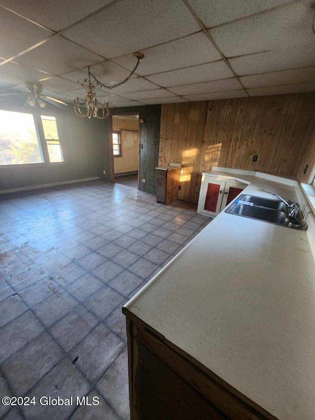 kitchen with ceiling fan, wooden walls, sink, and a drop ceiling