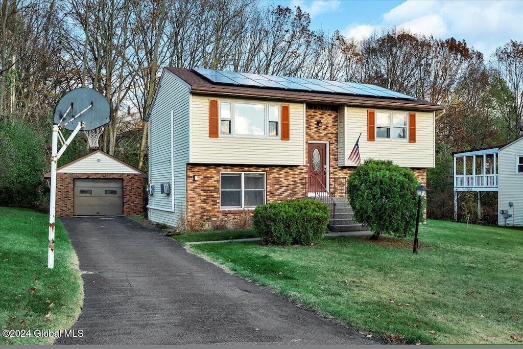 split foyer home with an outbuilding, a garage, a front yard, and solar panels