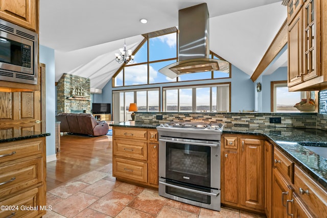 kitchen featuring an inviting chandelier, decorative backsplash, dark stone countertops, island range hood, and appliances with stainless steel finishes