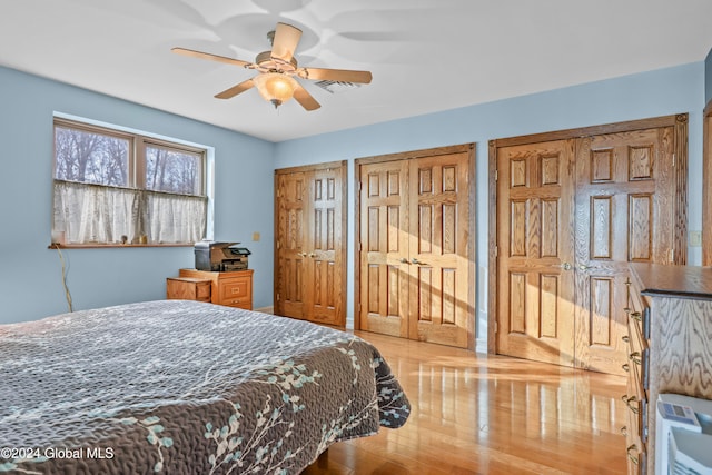 bedroom featuring light wood-type flooring, ceiling fan, and multiple closets