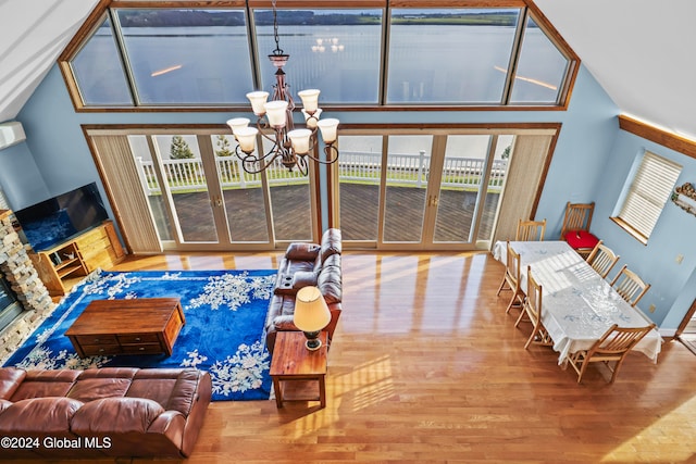 living room with a wealth of natural light, an inviting chandelier, high vaulted ceiling, and hardwood / wood-style flooring