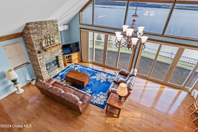 living room with a stone fireplace, light hardwood / wood-style flooring, high vaulted ceiling, and a chandelier