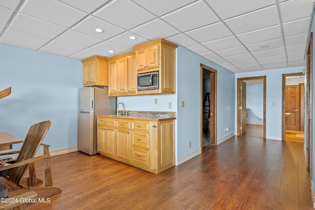 kitchen with appliances with stainless steel finishes, a paneled ceiling, sink, light brown cabinets, and hardwood / wood-style floors