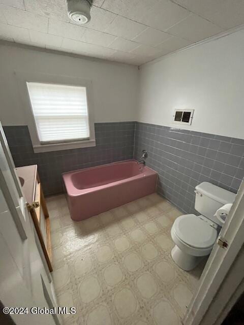 bathroom with a bath, tile walls, and toilet