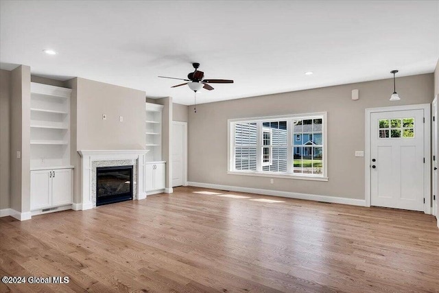 unfurnished living room featuring built in shelves, ceiling fan, and light hardwood / wood-style floors