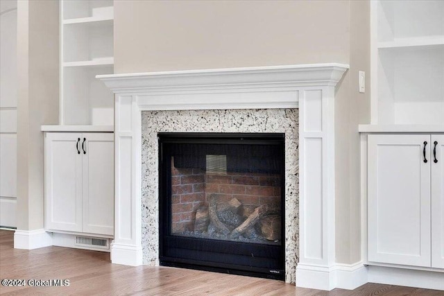 interior details featuring wood-type flooring, built in shelves, and a premium fireplace