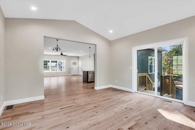 unfurnished living room with ceiling fan with notable chandelier, a healthy amount of sunlight, light hardwood / wood-style floors, and vaulted ceiling