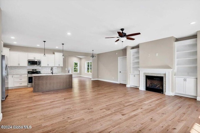 kitchen featuring white cabinets, a center island with sink, hanging light fixtures, light wood-type flooring, and stainless steel appliances