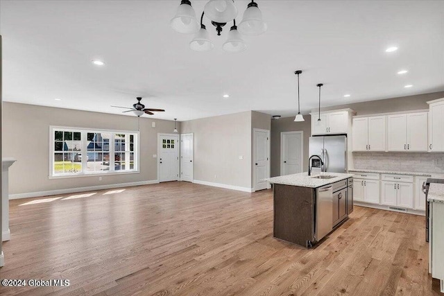 kitchen featuring white cabinetry, stainless steel appliances, hanging light fixtures, a center island with sink, and light wood-type flooring