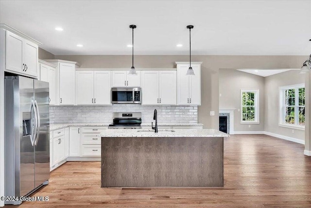 kitchen with pendant lighting, light stone countertops, appliances with stainless steel finishes, light hardwood / wood-style floors, and white cabinetry