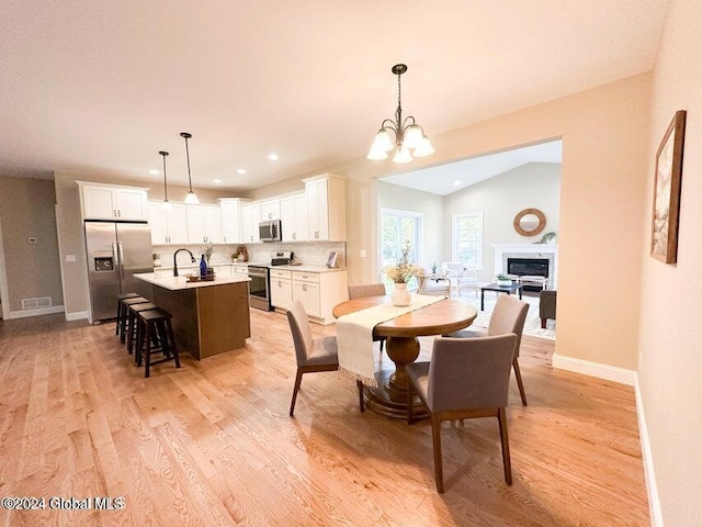 dining area featuring sink, a chandelier, lofted ceiling, and light wood-type flooring