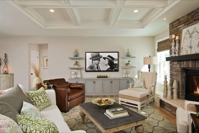 living room featuring coffered ceiling, a stone fireplace, light wood-type flooring, ornamental molding, and beam ceiling