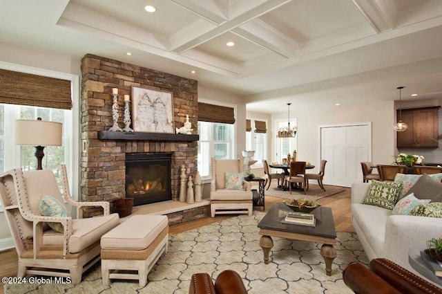 living room featuring coffered ceiling, a notable chandelier, beamed ceiling, a fireplace, and light hardwood / wood-style floors