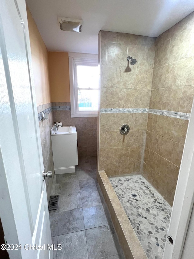 bathroom featuring a tile shower, vanity, and tile walls