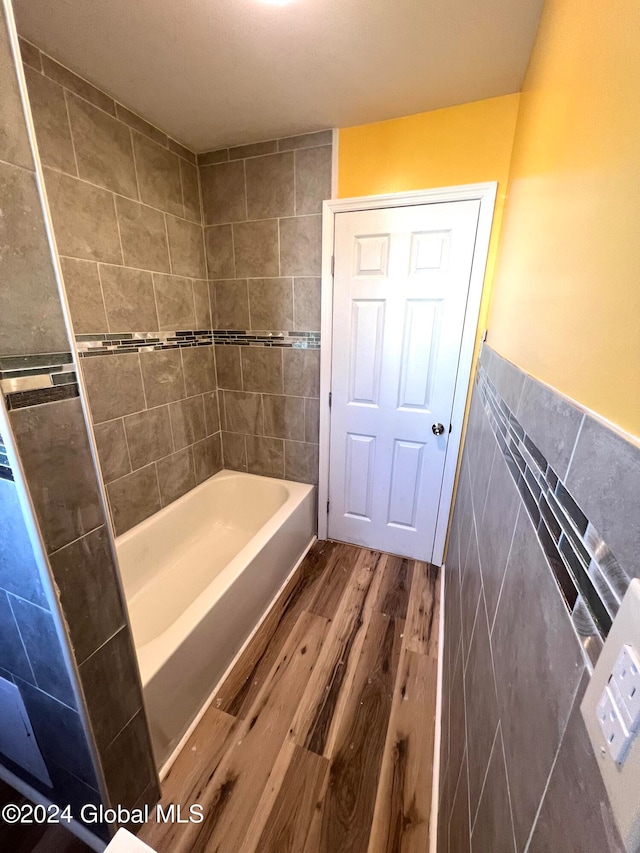 bathroom featuring wood-type flooring, tile walls, and tiled shower / bath