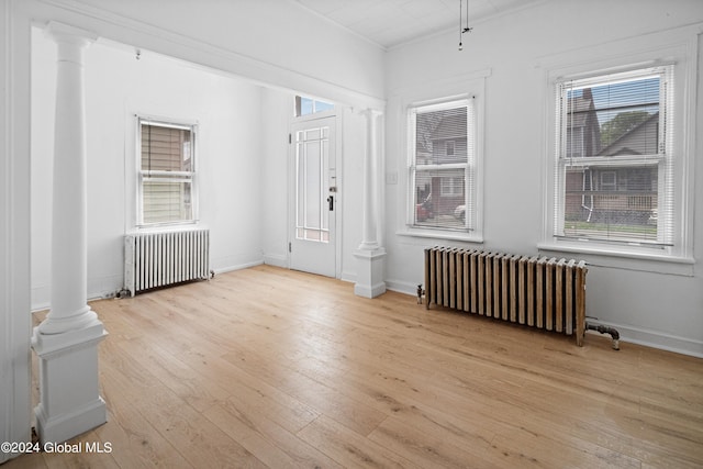 foyer entrance featuring light hardwood / wood-style floors, radiator heating unit, and decorative columns